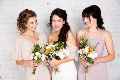 Bridal photoshoot of bridesmaids and bride wearing wedding dress with half updo and makeup holding flower bouquets