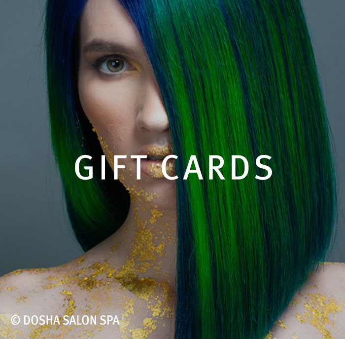 Model with vivid green and blue hair professionally cut and styled by master stylist Kristina Paris, featuring gold leaf makeup and artistic body detailing. Image represents creative hair color services, professional salon styling, and salon gift services available with Dosha Salon Spa gift cards.