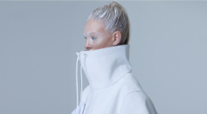 Image of Dosha Creative Team Photoshoot, Whiteout, with a model wearing frosty makeup and her hair tied back with a white coat that has a very high collar