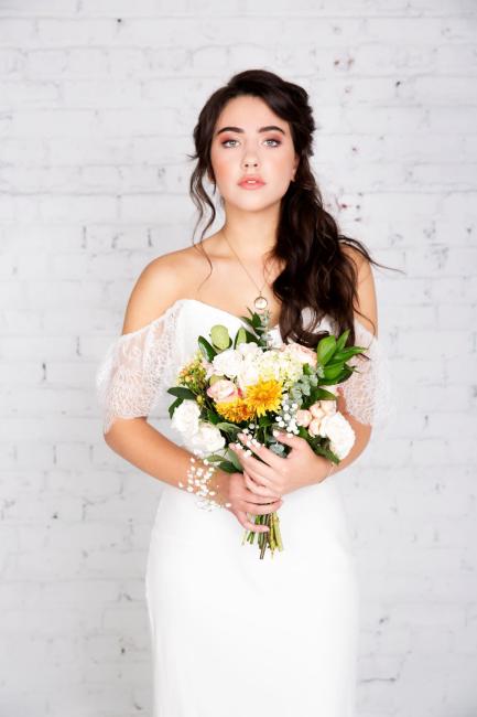 by the Bridal Elite Team Bridal photoshoot of bride wearing wedding dress with half updo and makeup holding a bouquet of flowers