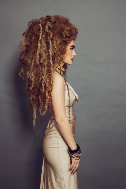 Photoshoot of model with circus inspired lion hairstyle and makeup in a tan dress with jewelry