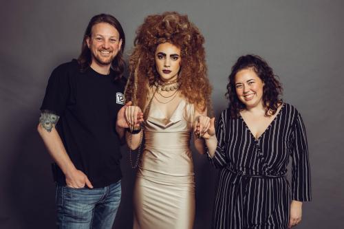 photoshoot of model posing with circus inspired lion hairstyle and makeup in tan dress with jewelry and stylists that created the look