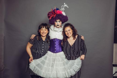 photoshoot of model posing in circus clown inspired makeup and hairstyle in a dress with heels with stylists who created the look