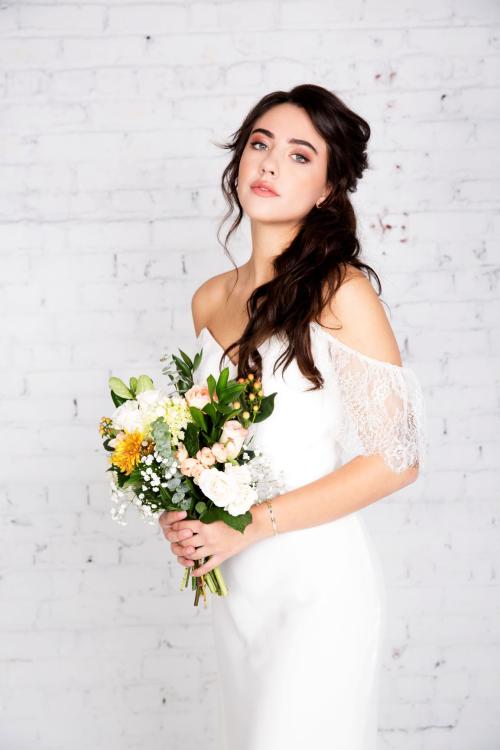 bridal photoshoot of bride wearing wedding dress with half updo and makup holding a bouquet of flowers