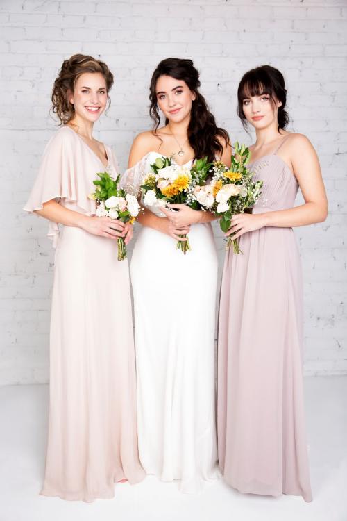 Bridal photoshoot of bride wearing wedding dress with half updo and makeup and bridesmaids holding bouquet of flowers