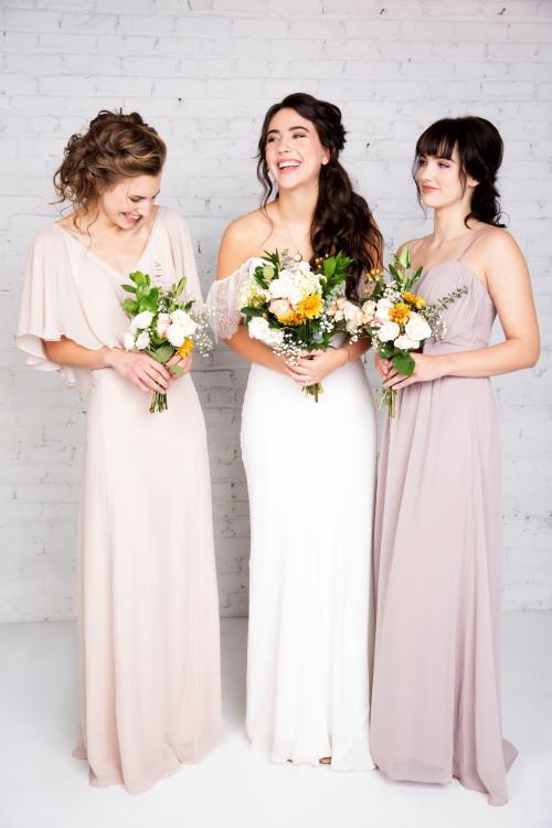 Bridal photoshoot of bride in wedding dress with half updo and makeup laughing with bridesmaids holding flower bouquets