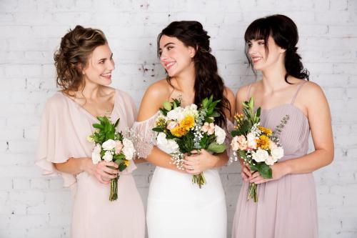 Bridal photoshoot of bride with half up do and makeup wearing wedding dress and bridesmaids holding flower bouquet