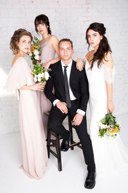 Bridal photoshoot of bride wearing wedding dress with half updo and makeup posing with groom in suit and tie and bridesmaids holding flower bouquets