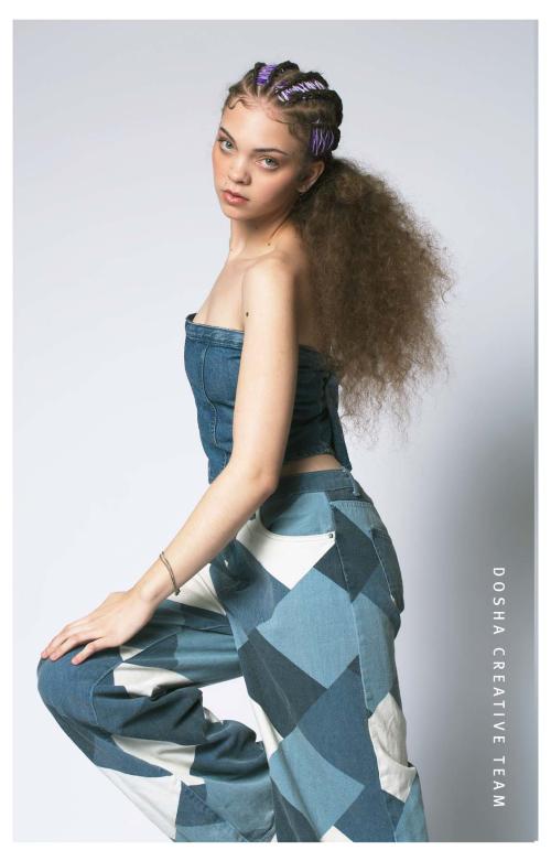 Braids x Denim photoshoot by Dosha Creative Team with a young woman wearing patchwork jean pants with a denim bodice and hair braided with purple at the top and made into a pony tail with her curls brushed out.