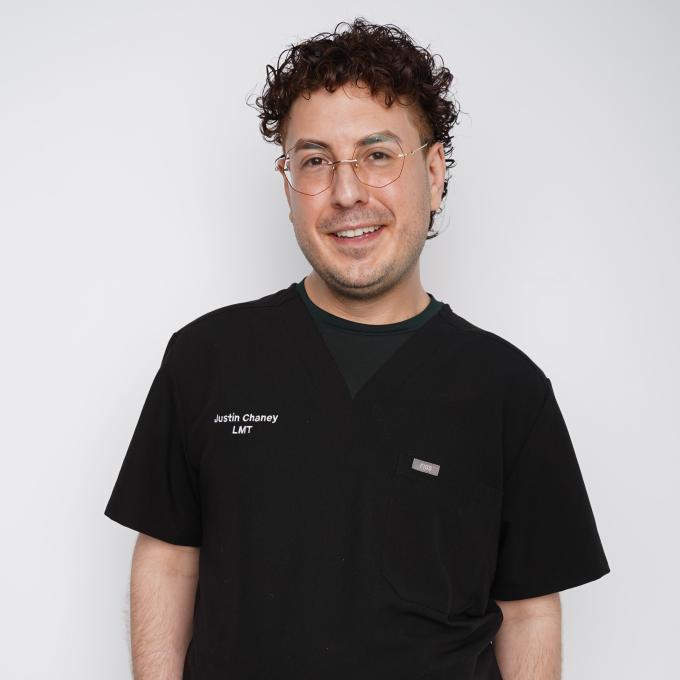 Massage therapist Justin smiling and wearing embroidered black scrubs